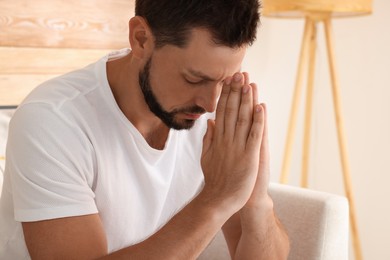 Religious man with clasped hands praying indoors