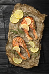 Photo of Tasty grilled salmon steaks and ingredients on black wooden table, top view