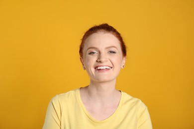 Candid portrait of happy red haired woman with charming smile on yellow background