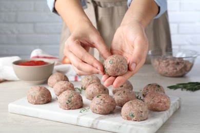 Photo of Woman making fresh raw meatballs at white table indoors, closeup