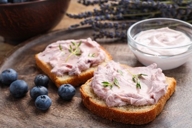 Tasty sandwiches with cream cheese, thyme and blueberries on wooden tray, closeup