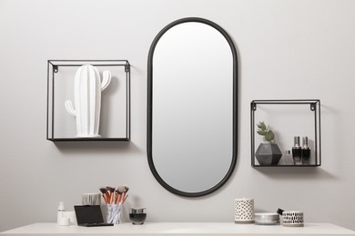 Stylish oval mirror hanging above dressing table with cosmetic products