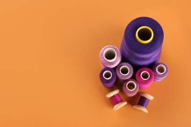 Different shades of violet and purple sewing threads on orange background, flat lay. Space for text