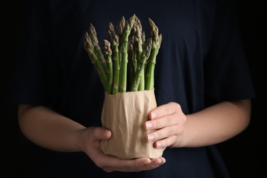 Woman with fresh asparagus on black background, closeup
