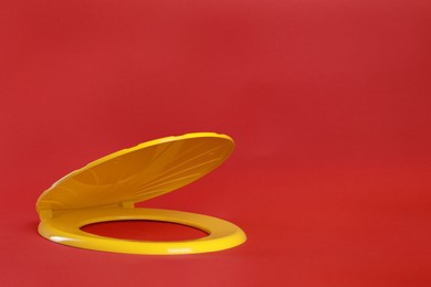 New yellow plastic toilet seat on red background, space for text