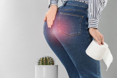 Woman with toilet paper sitting down on cactus against light grey background, closeup. Hemorrhoid concept