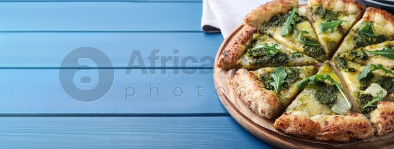 Delicious pizza with pesto, cheese and arugula on blue wooden table, space for text. Banner design