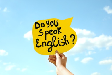 Woman holding paper speech bubble with question Do You Speak English against blue sky, closeup