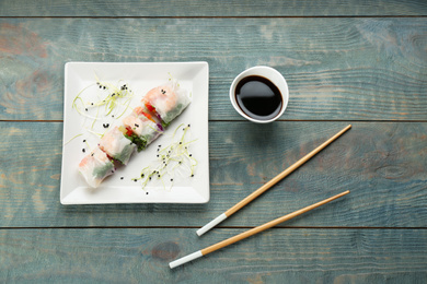 Delicious rolls wrapped in rice paper on light blue wooden table, flat lay