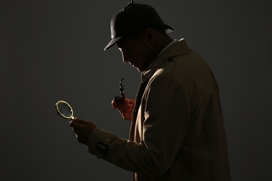Old fashioned detective with smoking pipe and magnifying glass on dark background