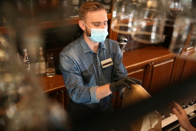 Waiter giving packed takeout order to customer in restaurant. Food service during coronavirus quarantine