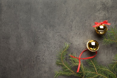 Golden sleigh bells and fir branches on grey background, flat lay. Space for text