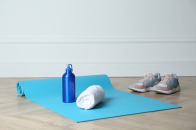 Photo of Exercise mat, towel, bottle of water and shoes on wooden floor indoors