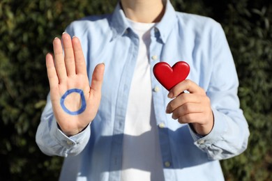 Woman showing blue circle as World Diabetes Day symbol and red heart outdoors, closeup