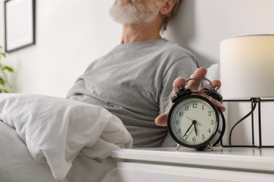 Photo of Man turning off alarm clock in bedroom, closeup