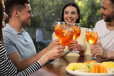 Friends clinking glasses of Aperol spritz cocktails at table