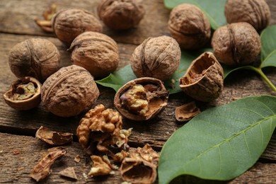 Whole and cracked walnuts with green leaves on wooden table, closeup