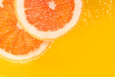 Slice of grapefruit in sparkling water on yellow background, closeup with space for text. Citrus soda