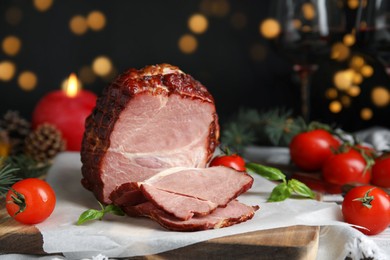 Delicious ham with tomatoes and basil on table against blurred festive lights, closeup. Christmas dinner