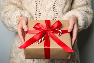 Woman holding Christmas gift box on grey background, closeup