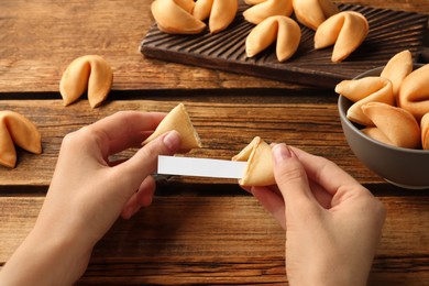 Photo of Woman holding tasty fortune cookie with prediction at wooden table, closeup. Space for text