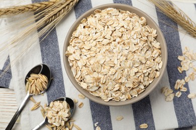 Photo of Bowl of oatmeal, spoons, napkin and spikelets on white wooden table, flat lay