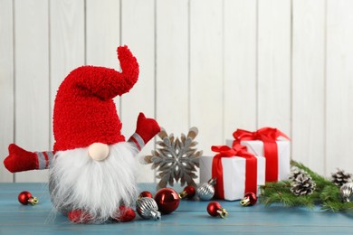 Cute Christmas gnome, gift boxes and festive decor on turquoise table against white wooden background