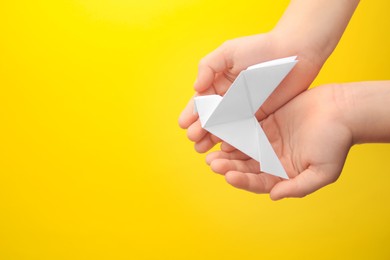 Photo of Origami art. Child holding paper bird on yellow background, top view. Space for text
