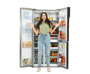 Excited young woman near open refrigerator on white background