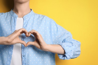 Woman making heart with hands on yellow background, closeup. Space for text