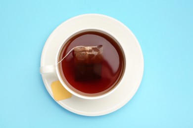 Tea bag in cup of hot water on light blue background, top view