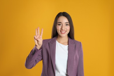 Woman in violet blazer showing number three with her hand on yellow background