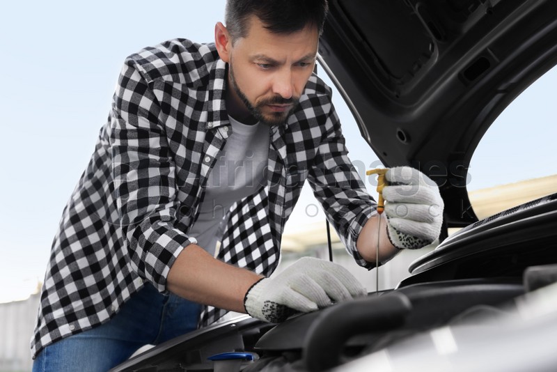 Photo of Man checking motor oil level with dipstick in car outdoors