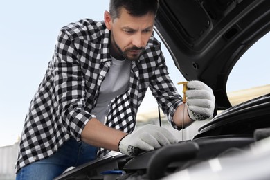 Man checking motor oil level with dipstick in car outdoors