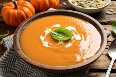 Tasty creamy pumpkin soup with basil in bowl on wooden table