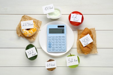 Calculator and food products with calorific value tags on white wooden table, flat lay. Weight loss concept
