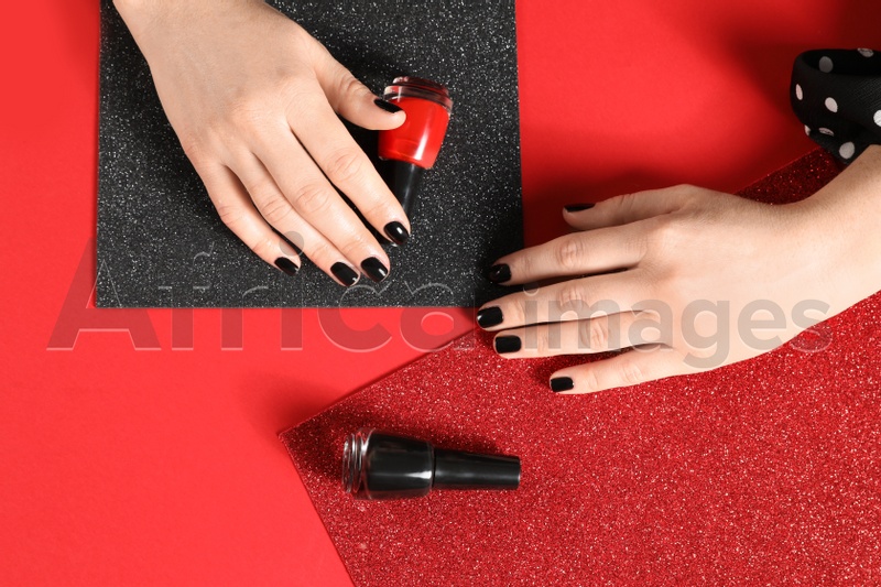 Woman with black manicure and nail polish bottles on color background, top view