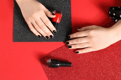 Woman with black manicure and nail polish bottles on color background, top view