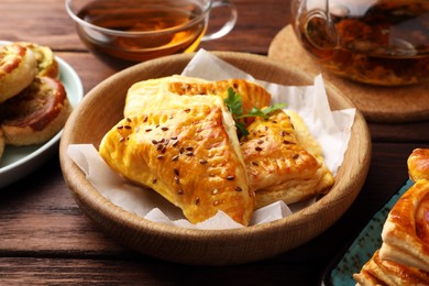 Photo of Fresh delicious puff pastry served with tea on wooden table, closeup