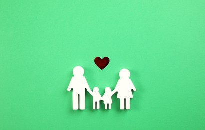 Family figure and red heart on green background, flat lay