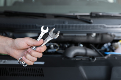 Professional auto mechanic holding wrenches near modern car in service center, closeup of hand
