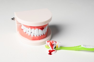 Photo of Toothbrush with paste and blood near jaw model on white table. Gum inflammation