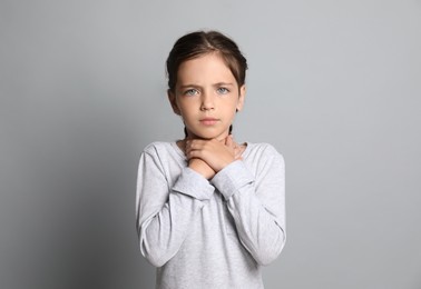 Little girl suffering from sore throat on grey background
