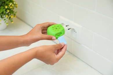 Woman putting insect repellent plate into electric mosquito device at home, closeup