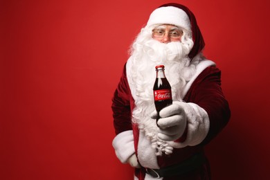 MYKOLAIV, UKRAINE - JANUARY 18, 2021: Santa Claus holding Coca-Cola bottle on red background, space for text