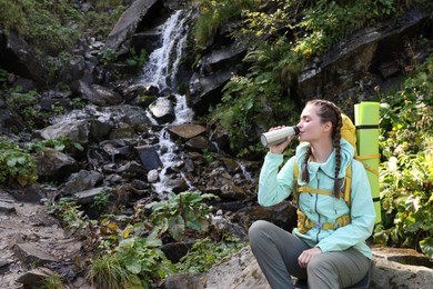 Tourist with vacuum flask near waterfall in mountains. Space for text