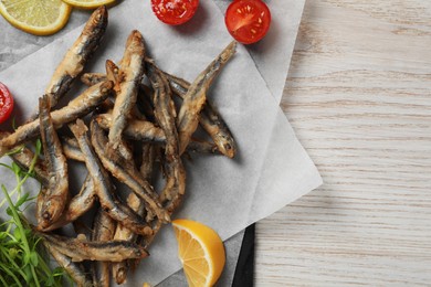 Photo of Slate board with delicious fried anchovies, lime and tomatoes on white wooden table, top view