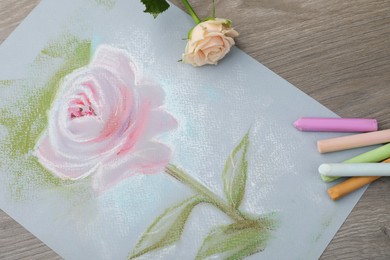 Beautiful drawing of pink rose, fresh flower and pastels on wooden table, flat lay