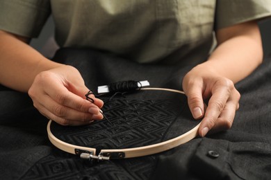 Woman embroidering black shirt with thread in hoop, closeup. Ukrainian national clothes