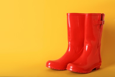 Pair of red rubber boots on orange background. Space for text